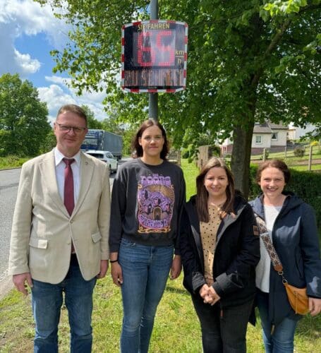 Der Bürgermeister von Waldkappel, Frank Koch, und die Abgeordnete Karina Fissmann, begleitet von zwei Elternteilen, vor dem neu installierten Geschwindigkeitsanzeigegerät EVOLIS Vision in Bischhausen.